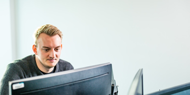 computer student sat at a dual monitor desk
